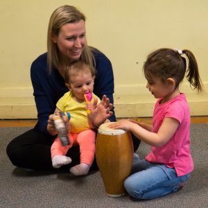 A mom and two kids learn to play the conga at a Rainbow Songs class
